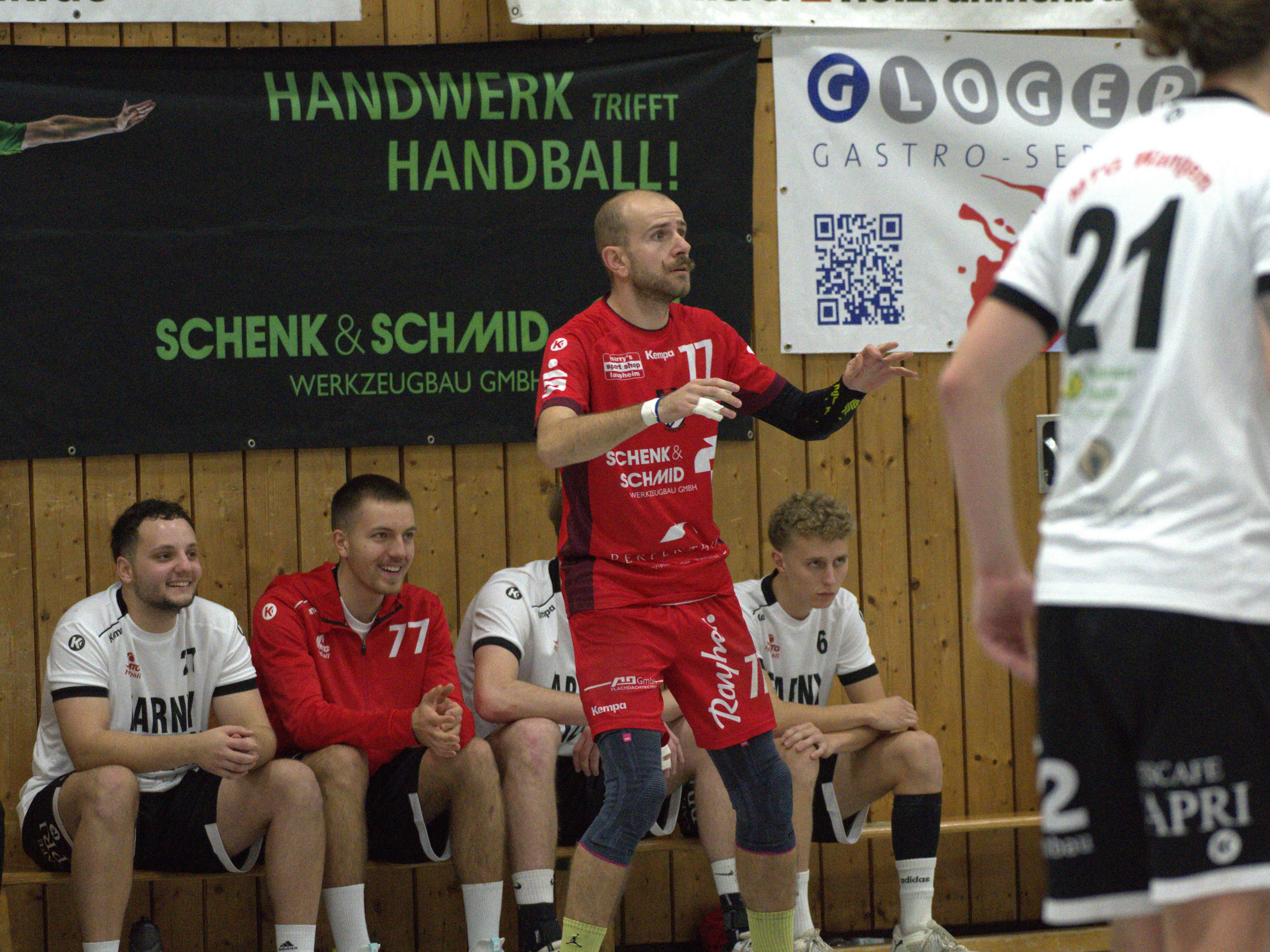 Im Fokus ist der Spieler mit der Trikotnummer 77 des HRW-Laupheim, dahinter sitzen vier Spieler des TV Altenstadt auf der Bank.