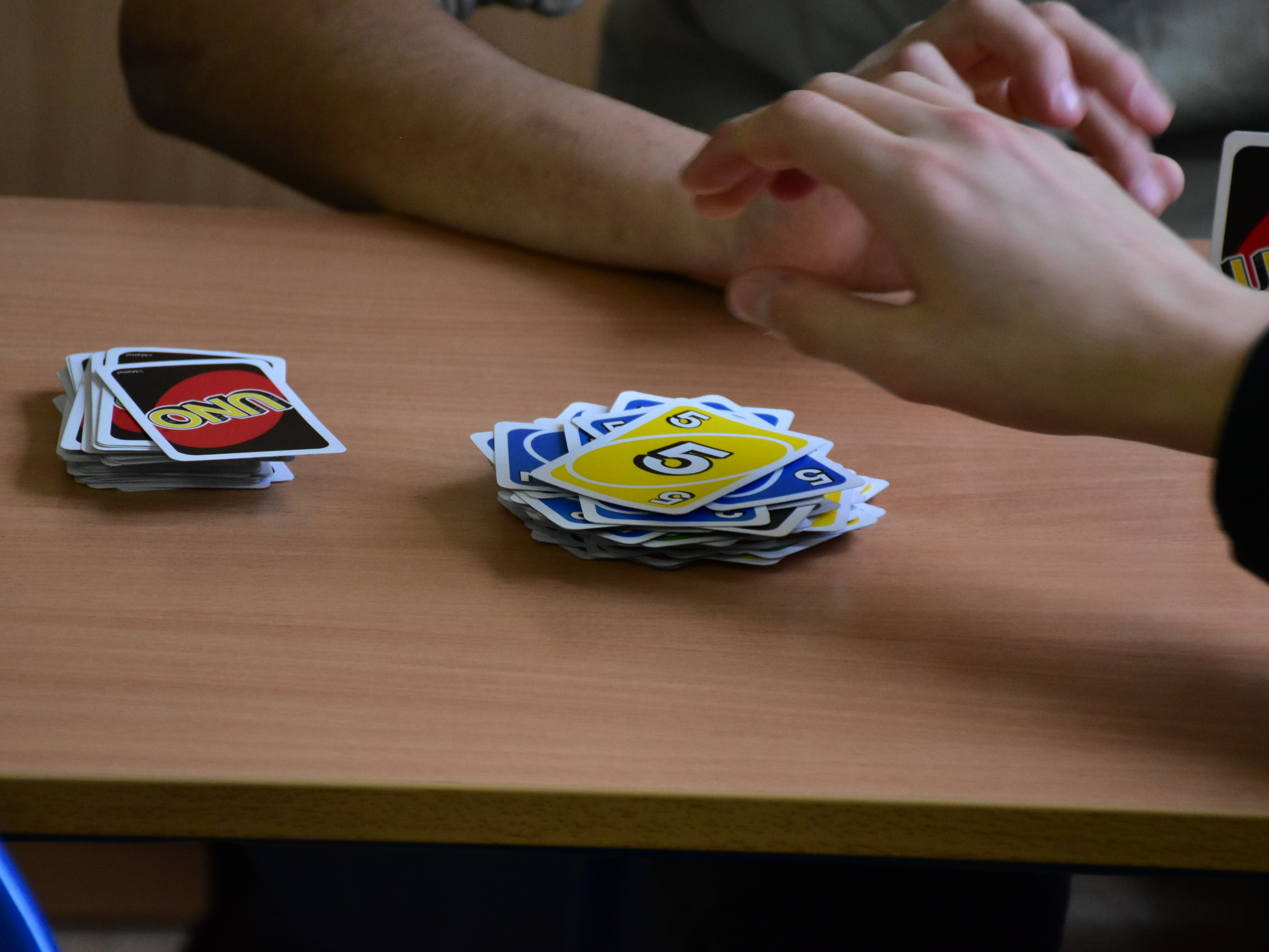 Andrzejkowe wróżby i nie tylko. | Zbliżenie na dwa stosiki kart do uno. Nad nimi dłoń sięgająca po kartę..JPG