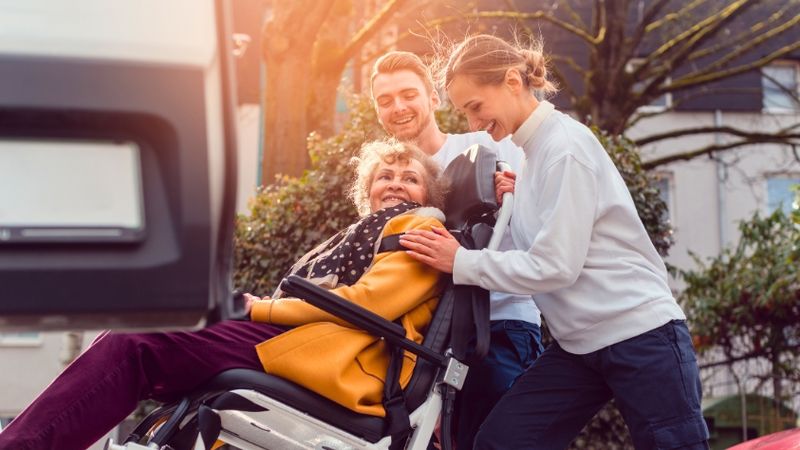 Vrouw in rolstoel wordt in een busje geholpen