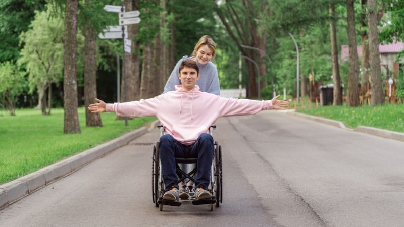 Vrouw duwt een jongen, in een rolstoel, die beide kanten op wijst