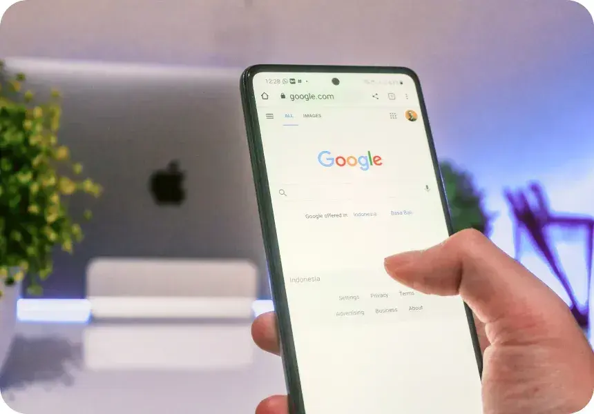 Hånd som holder en mobiltelefon med Googles søkemotor på skjermen.