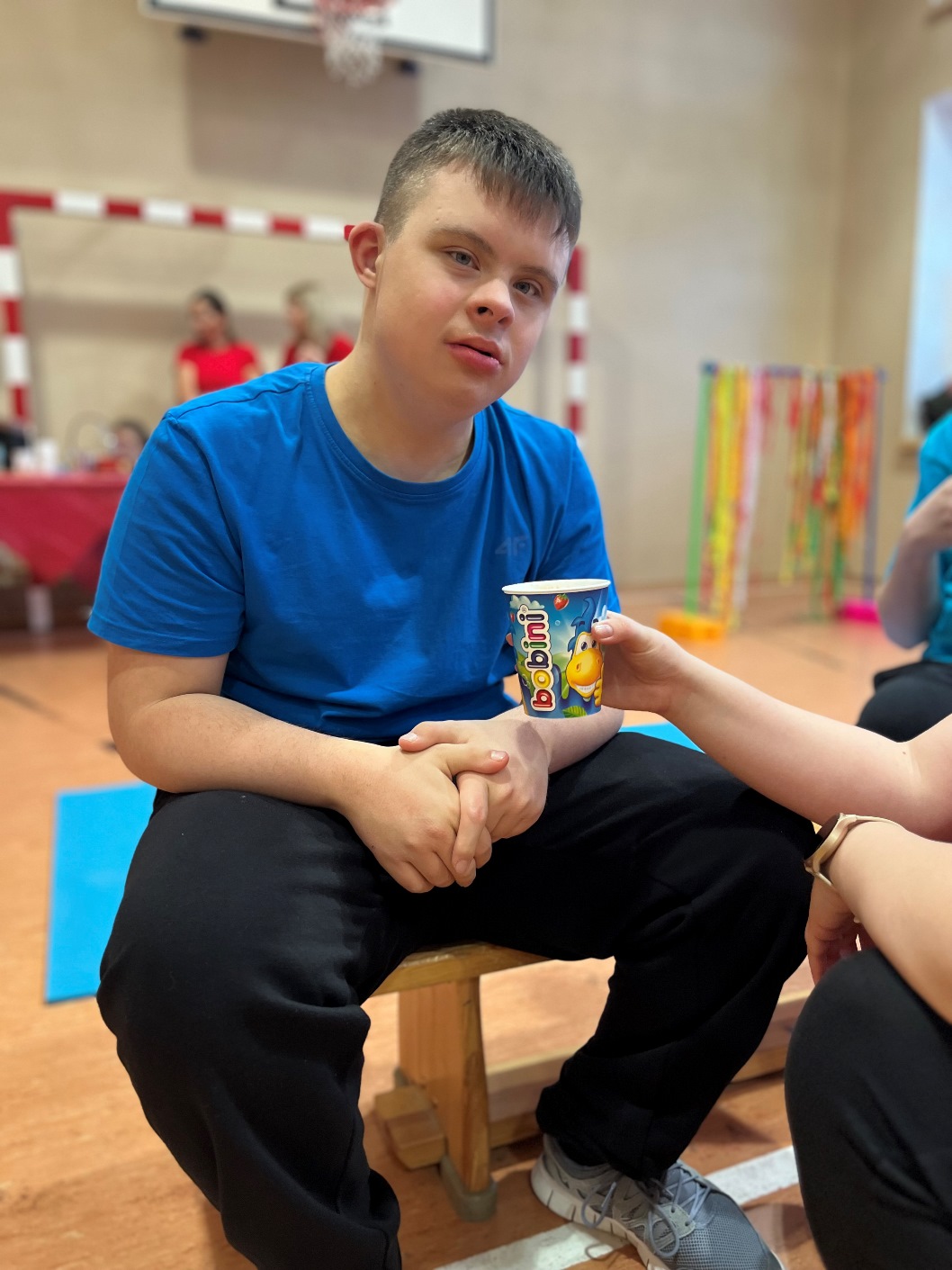 Dzień treningowy | Chłopak siedzi na ławce, ktoś podaje mu kubek.JPG