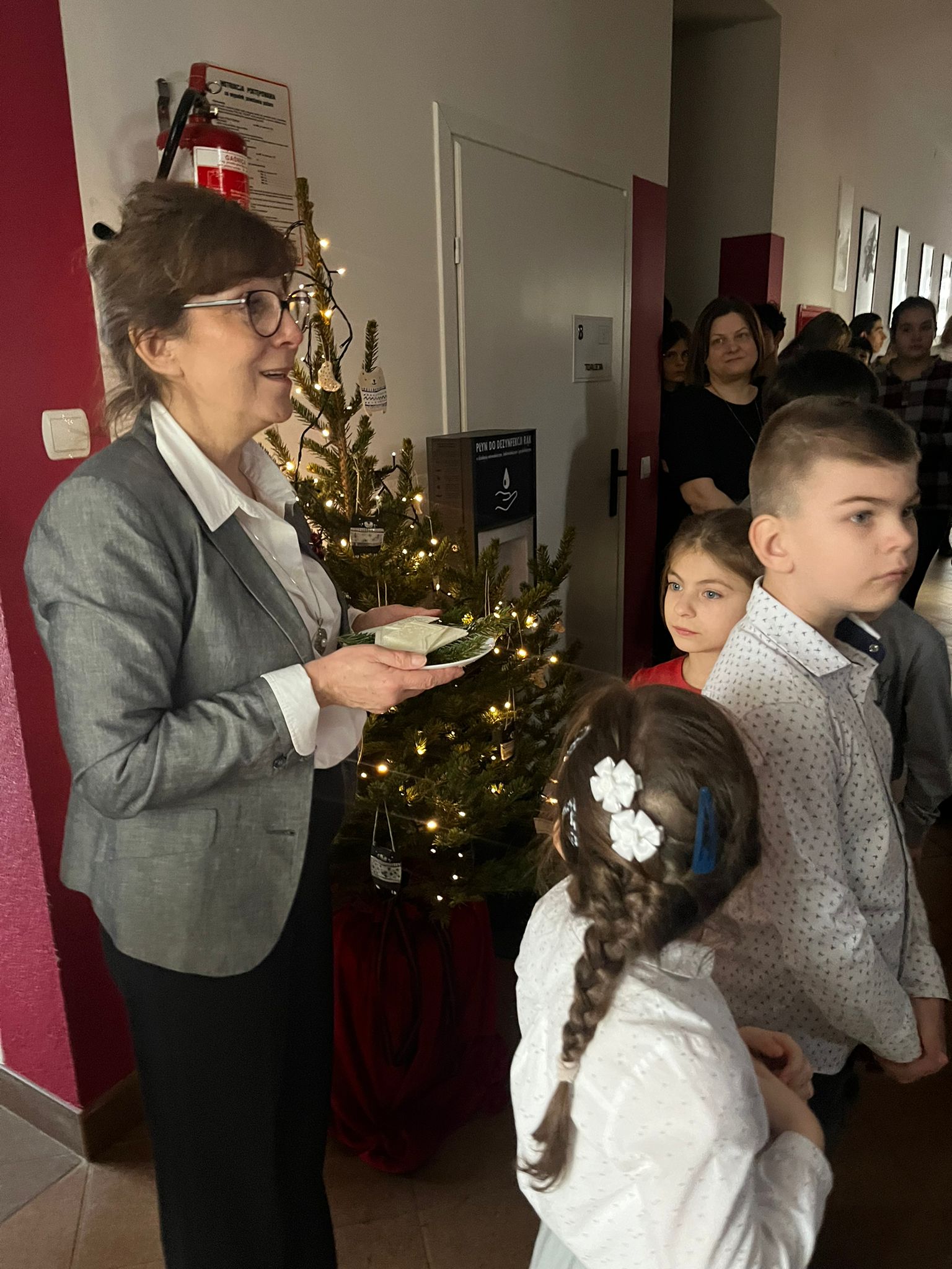 Nasz szkolny chór Karolus, zawsze obecny podczas uroczystości i wydarzeń muzycznych w naszym środowisku, zdobywa również uznanie na zewnątrz, biorąc udział w festiwalach i konkursach.  Gratulujemy wszystkich osiągnięć, zwłaszcza tych ostatnich, jakimi było zdobycie pierwszych miejsc na XI Wojewódzkim Festiwalu Piosenki Patriotycznej, Żołnierskiej i Harcerskiej Placówek Kształcenia Specjalnego w Rudniku nad Sanem oraz IX Wojewódzkim Festiwalu Dzieci i Młodzieży z Niepełnosprawnością Intelektualną w Dębicy.  Jesteśmy z was dumni! | Dyrektorka trzyma opłatek, przd nią uczniowie.jpg