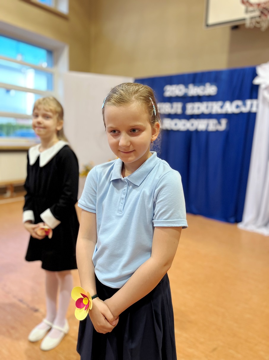 Świętujemy Dzień Edukacji Narodowej | Dziewczynka w niebieskiej koszulce i kotylionem na ręce stoi na scenie .JPG