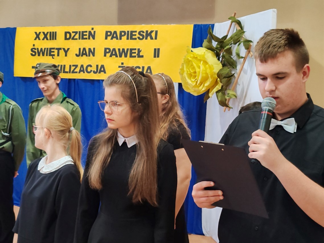 DZIEŃ PAPIESKI | Uczeń czyta do mikrofonu na scenie.jpg