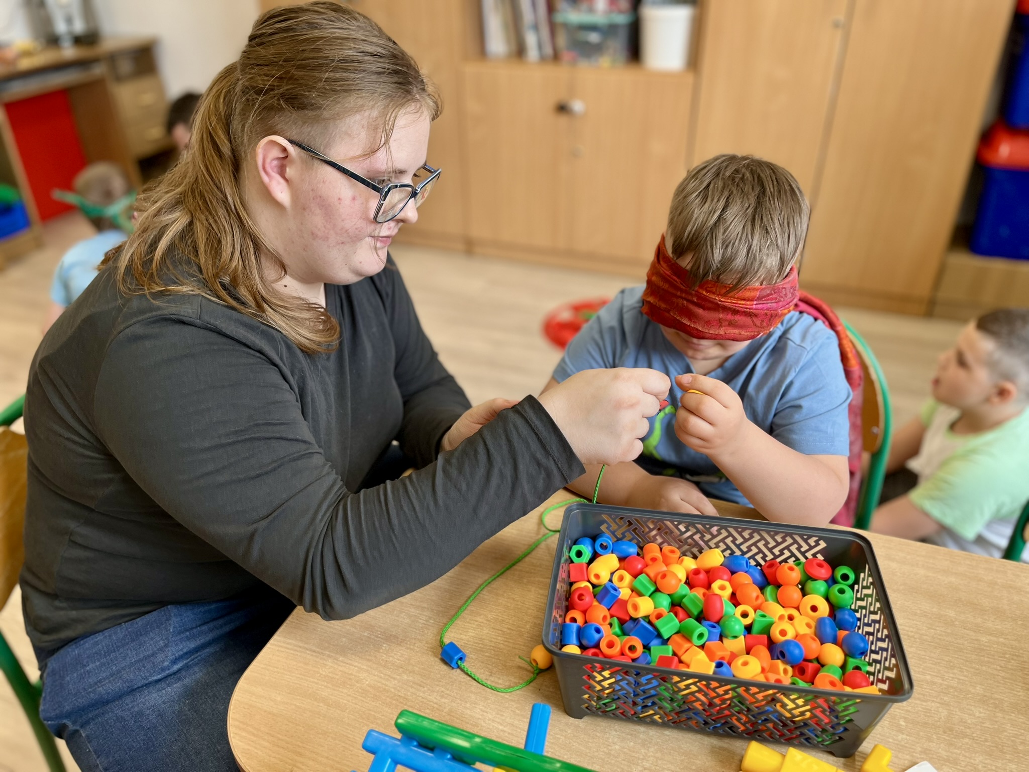 Jesteśmy różni i pomagamy sobie | Uczennica i uczeń z chustą na oczach nawlekają korale na sznurek.JPEG