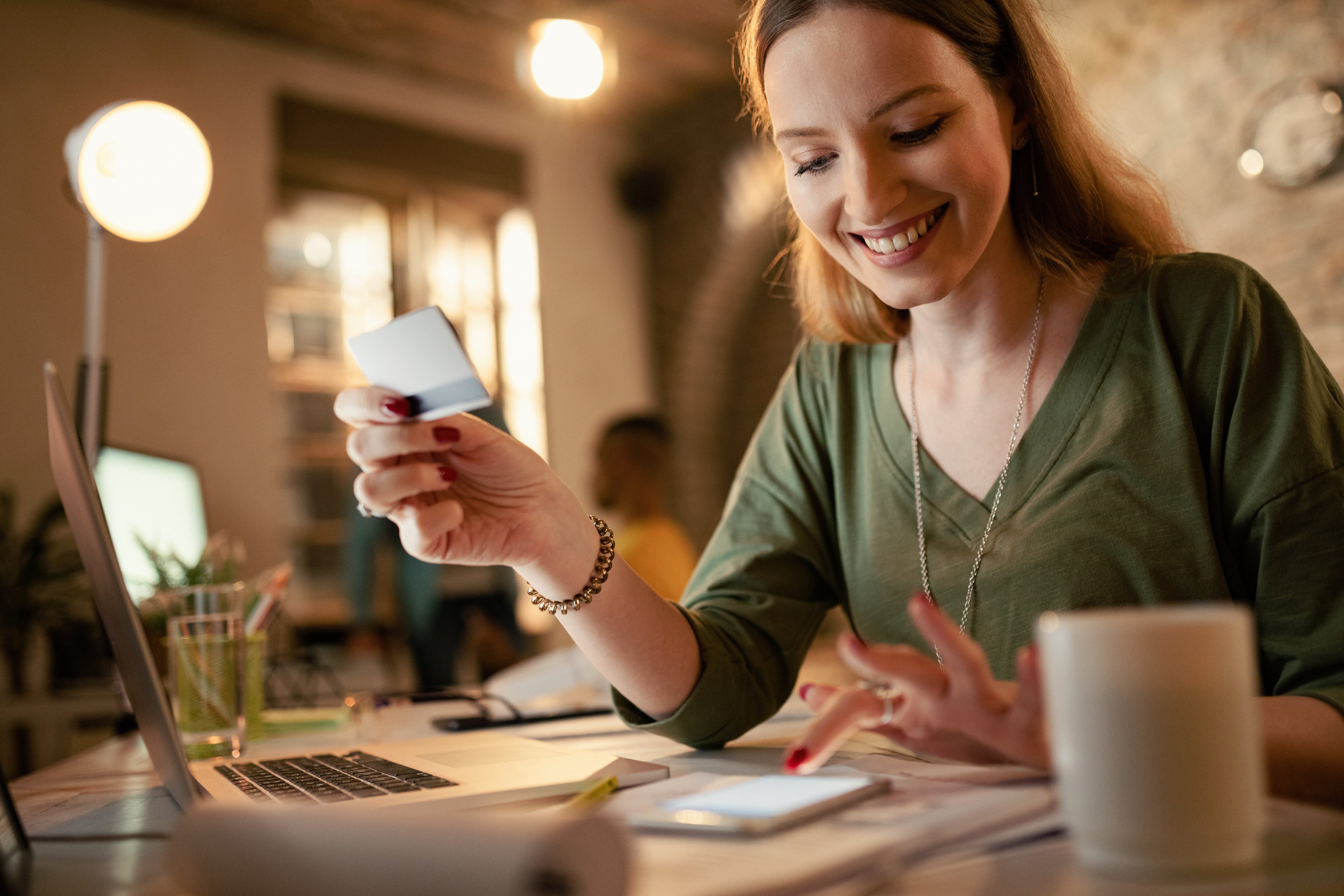 happy-businesswoman-using-smart-phone-credit-card-while-shopping-internet-night-office.jpg