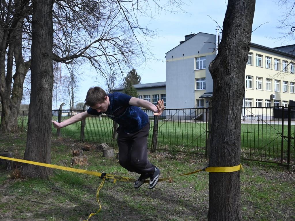 Czekając na Święta | Chłopiec wybija się do skoku z naciągniętej między pniami drzew żółtej taśmy.JPG