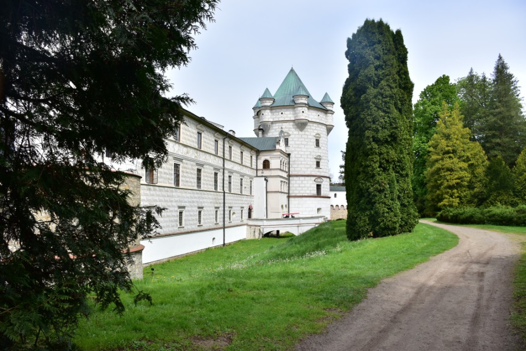 Przemyśl i okolice | Pałac z białego kamienia widziany w perspetywie, z wieżą na końcu. Z przodu fragment dużego krzewu, w tle drzewa i krzewy..JPG