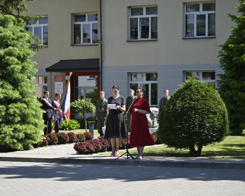 Święto Szkoły- XVII rocznica nadania imienia Jana Pawła II | Fragment placu szkoły z kamiennym obeliskiem, przy którym wartę przymają harcerze. Obok stoi poczet sztandarowy. Z przodu dwie kobiety, jedna z nich przemawia do mikrofonu.JPG