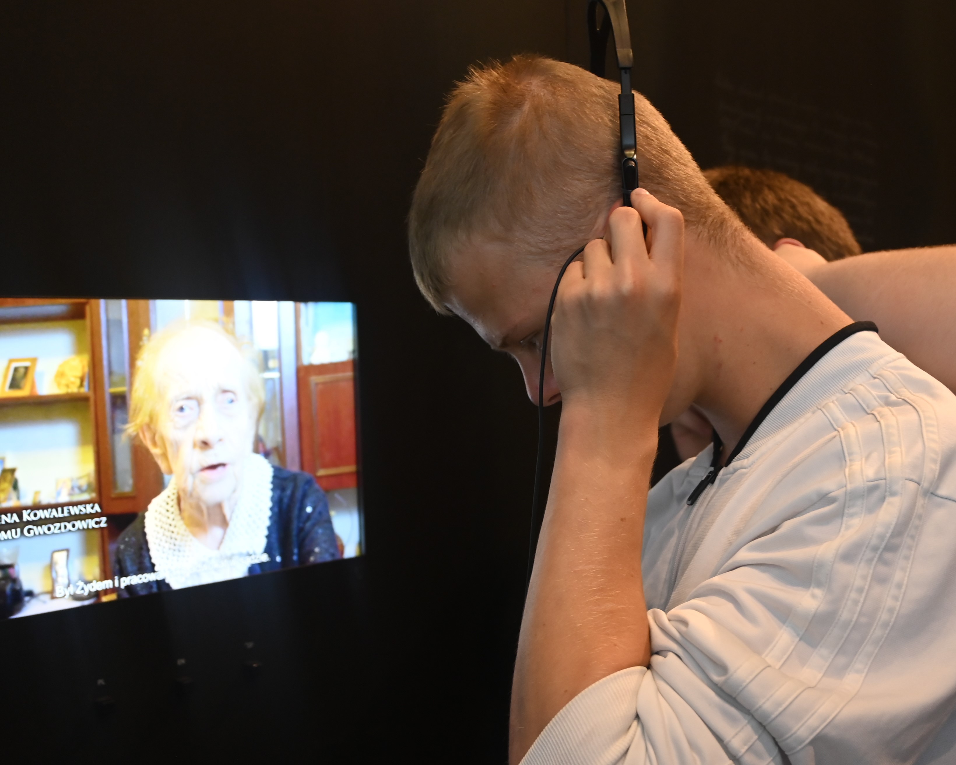 Wycieczka do Markowej | Profil chłopca z pochyloną głową przytrzymującego dłońmi słuchawki na uszach. W tle ekran telewizora z wyświetlanym filmem..JPG