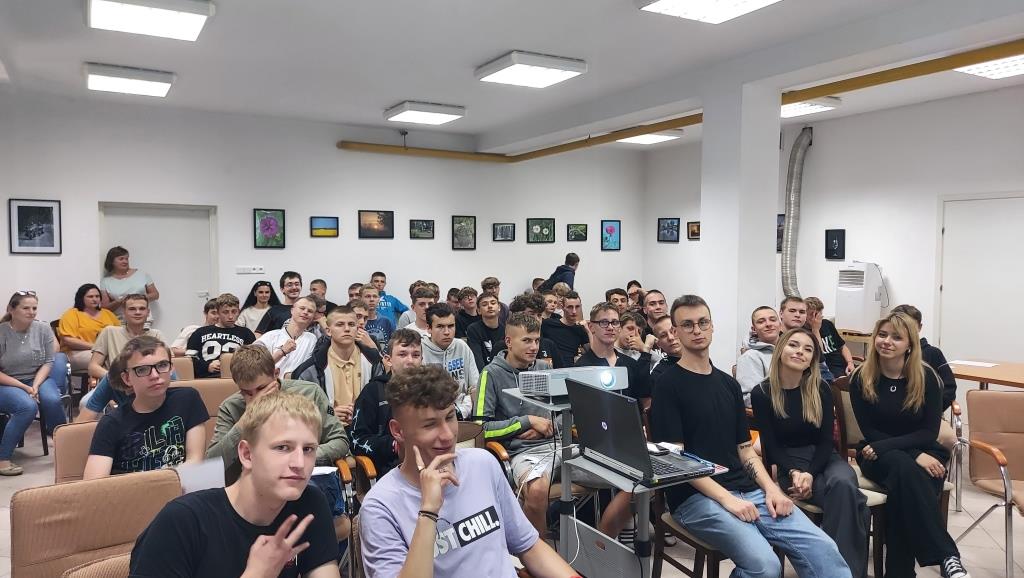 Spotkanie „Twarze sukcesu” | Ogólny widok sali - na krzesłach siedzą chłopcy z MOW, w pierwszym rzędzie siedzą studenci prowadzący spotkanie. Obok nich na stoliku laptop i rzutnik.jpg