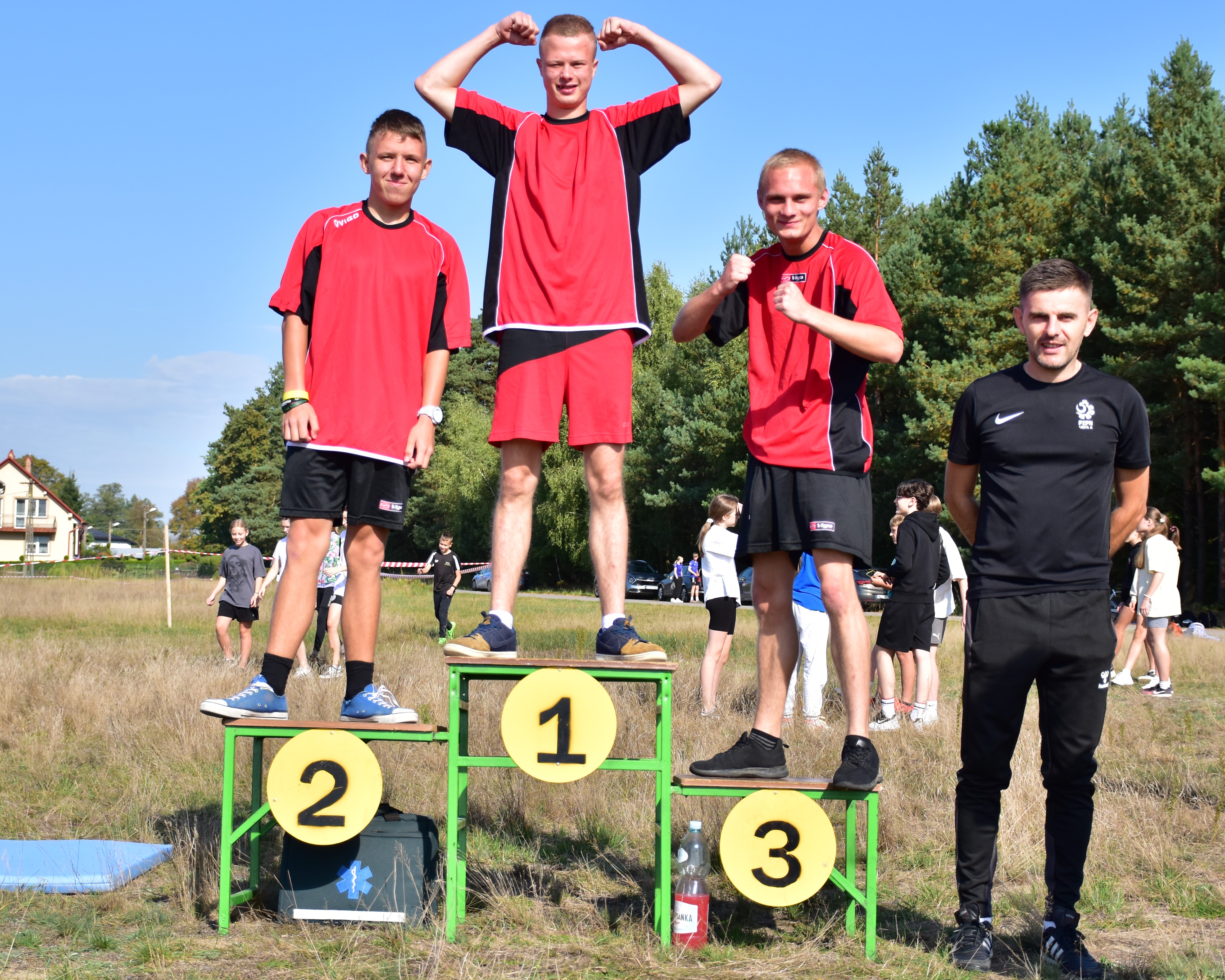 Bierzemy udział w XXIX Biegu im. Generała Stanisława Dąbka | W lesie, na tzw. pudle , czyli podium stoją trzej wychownkowie MOW. Ubrani w jednakowe stroje sportowe. obok nich po lewej stronie stoi ich wych — kopia.JPG