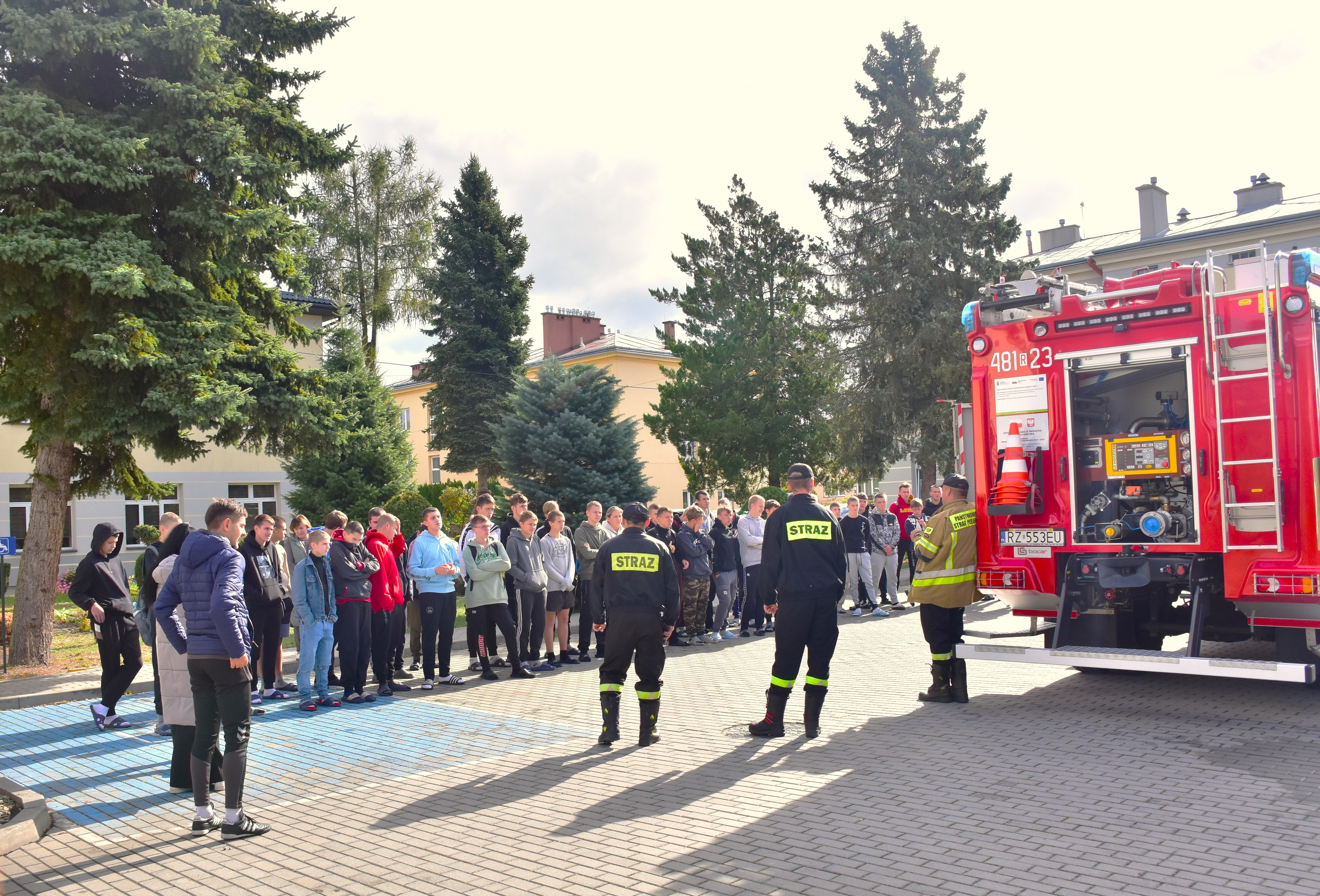 Wizyta Państwowej Straży Pożarnej | Na placu szkolnym stoja w dwuszeregu wychowankowie MOW wraz z nuczycielemi. Przed nimi wóz strażacki z otwartymi  ścianami oraz umundurowani strażacy opowiadający o wypozaśeniu wozu..JPG