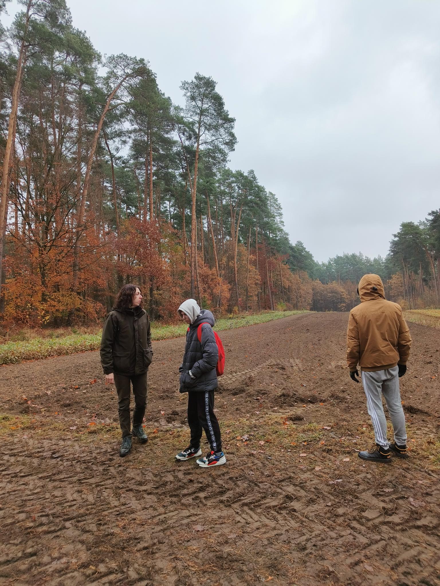 Kariera bez barier  | Na świeżo zaoranej polanie, otoczonej z trzech  stron wysokim lasem stoi pani leśnik oraz wychowankowie. Kobieta w stroju leśnika, zwrócona trar.jpg