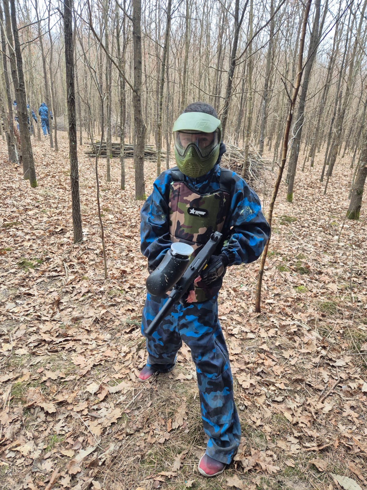 PAINTBALL | W lesie w pełnym umundurowaniu stoi wychowanek trzymający pistolet do paintbaalu..jpeg