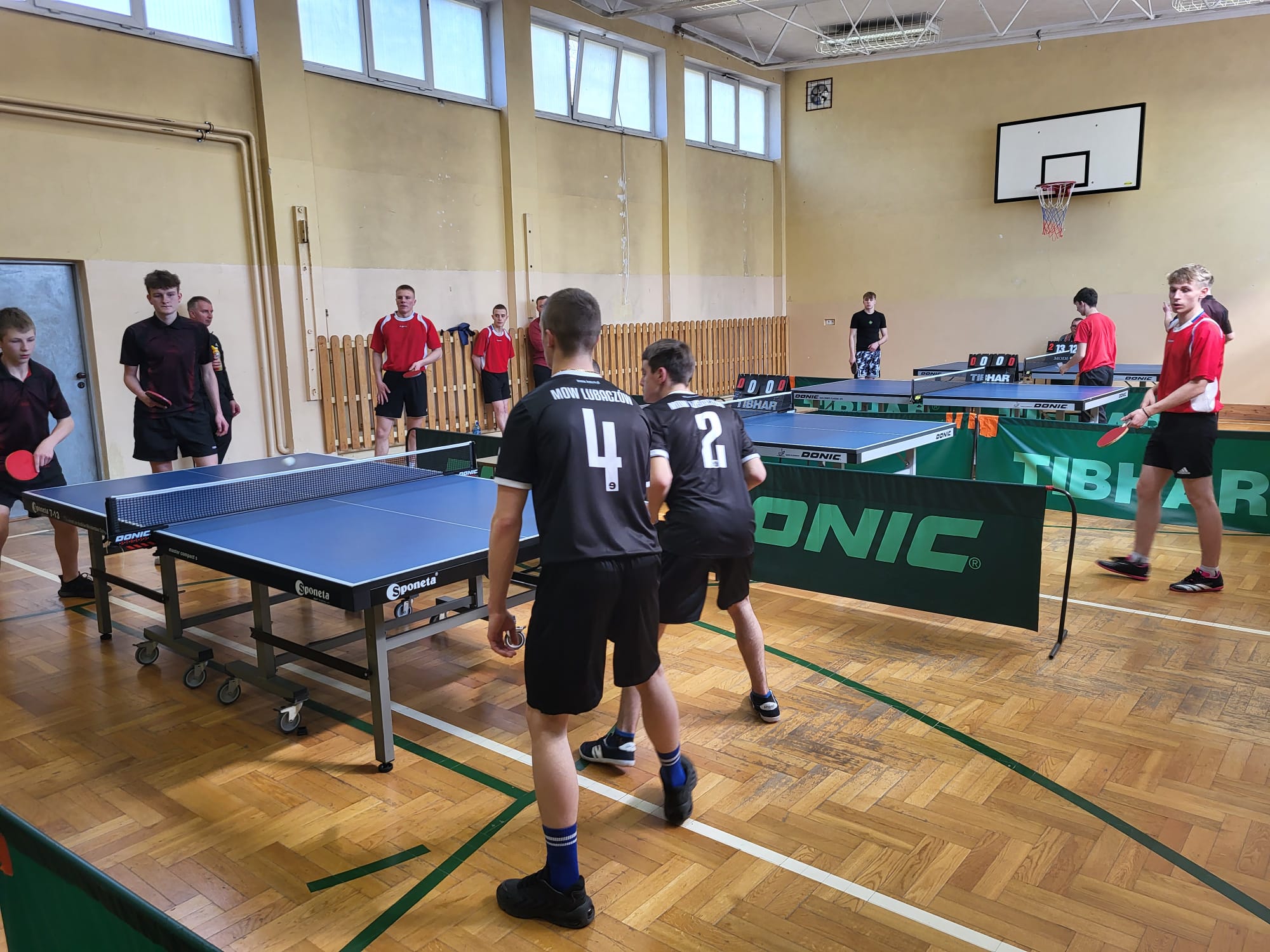 Turniej Eliminacyjny XXXIX Mistrzostw Polski MOW w Tenisie Stołowym  | W sali gimnastycznej są rozstawoine jeden obok drugiego czrery stoły do tenisa, które są oddzielone za pomocą barierek. Przy każdym ze stołów gra po czterech zawodników..jpg