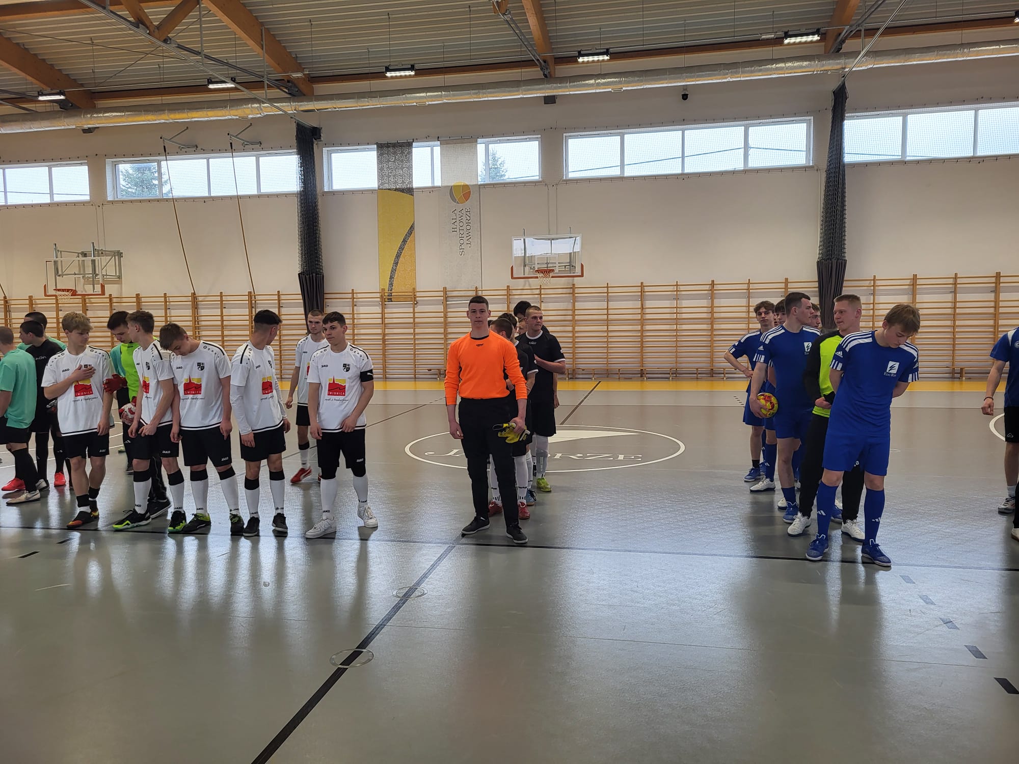 Turniej Eliminacyjny Mistrzostw Polski w Halowej Piłce Nożnej  | W nowoczesnej hali sportowej stoi pięć drużyn sportowych. Każda z drużyn ma swoje stroje, które sie odróżniają. Dryżyny ustawione są rzędmi gęsiego, tzn jeden za drugim,..jpg