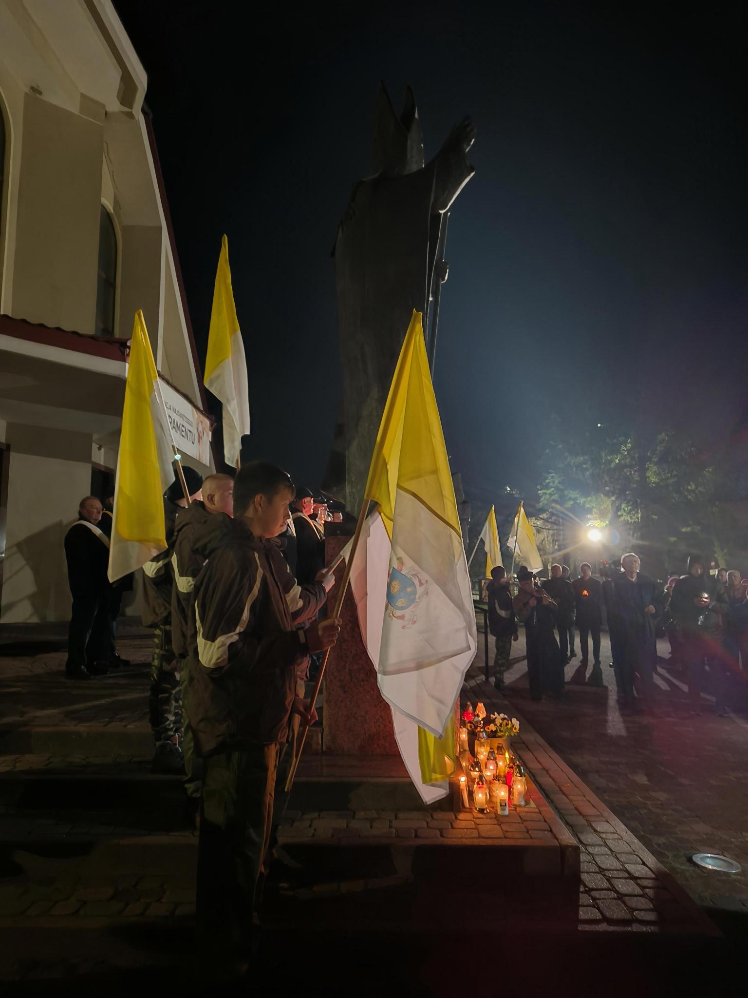 XX Rocznica śmierci św. Jana Pawła II | Zdjęcie pomnika św. Jana Pawła II w otoczeniu harcerzy z naszego ośrodka. Którzy stoją w pełnym umundurowaniu wokół pomnika trzymając w rękach flagi papieskie..jpg