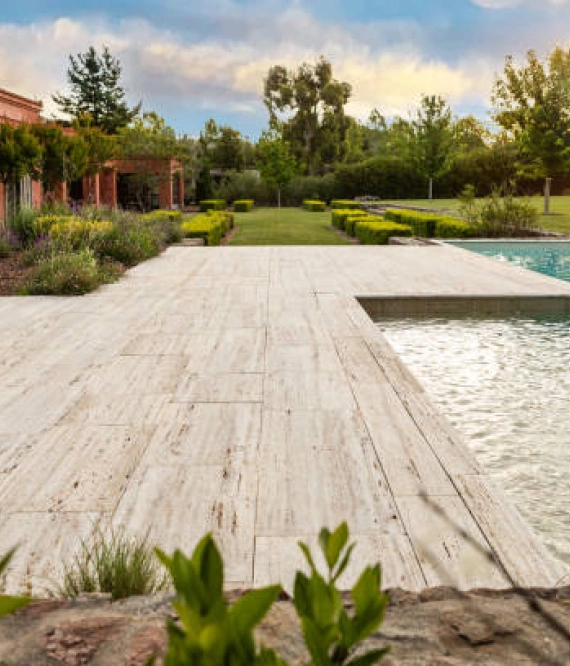 Ein Holzdeck an einem Pool mit einem großen Garten im Hintergrund