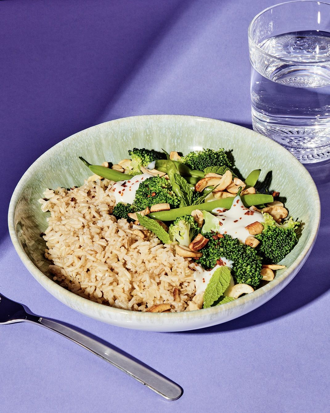 Schüssel mit gekeimtem Bio-Naturreis, grünem Gemüse wie Brokkoli und Zuckerschoten, getoppt mit cremigem Joghurt-Dressing und gerösteten Nüssen.
