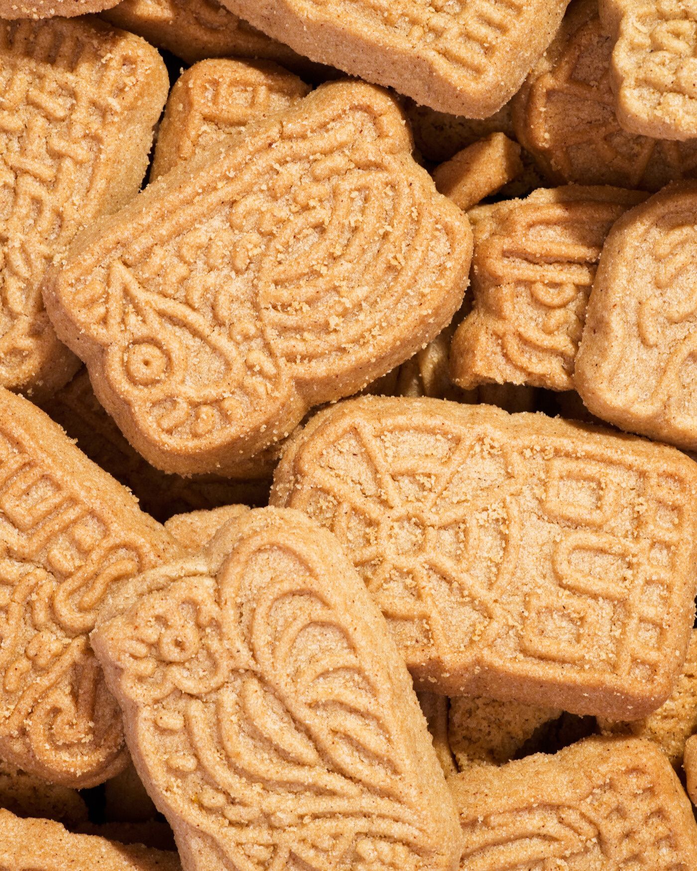 Nahaufnahme einer Fülle von goldbraunen Spekulatius-Keksen, die übereinander gestapelt sind. Die Kekse haben die typischen, fein geprägten und unterschiedlichen Winter- oder Weihnachtsmotive.