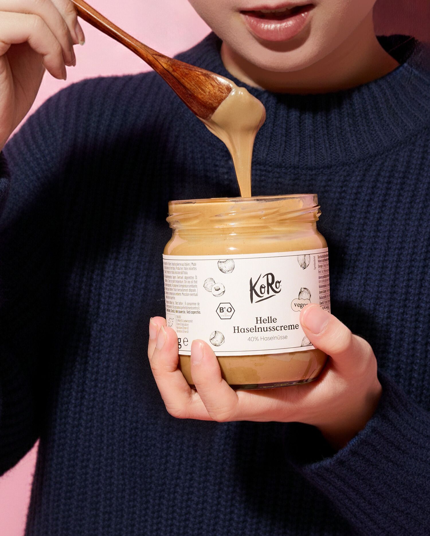 Nahaufnahme einer Person in einem dunkelblauen Strickpullover, die ein Glas 