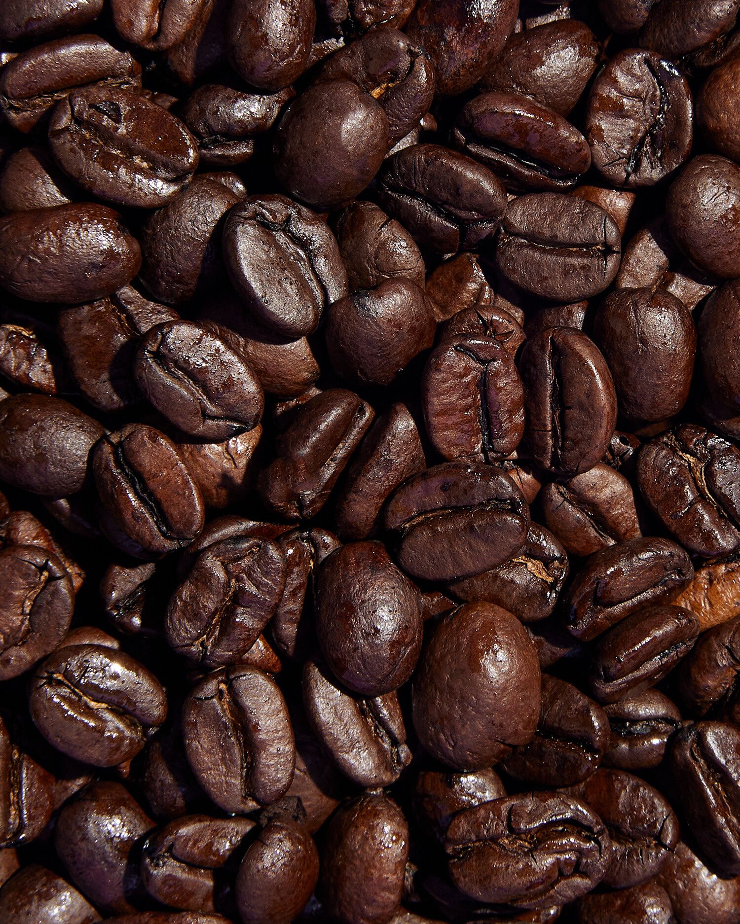 Eine Nahaufnahme von dunkel gerösteten Kaffeebohnen, die dicht beieinander liegen.