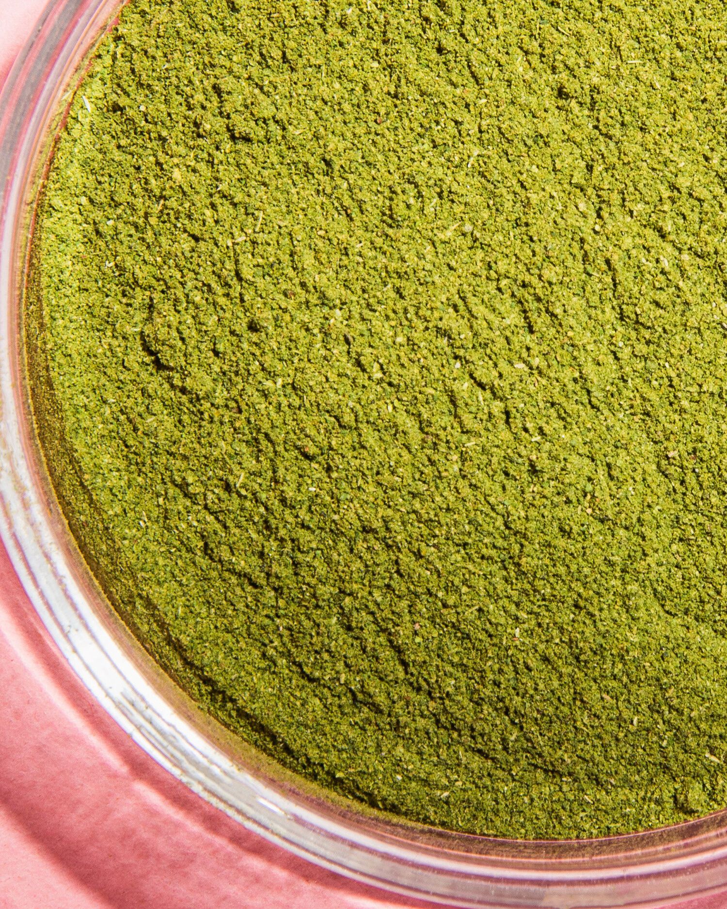 Nahaufnahme von leuchtend grünem Spinatpulver in einem durchsichtigen Glas, das auf einer rosa Oberfläche steht.