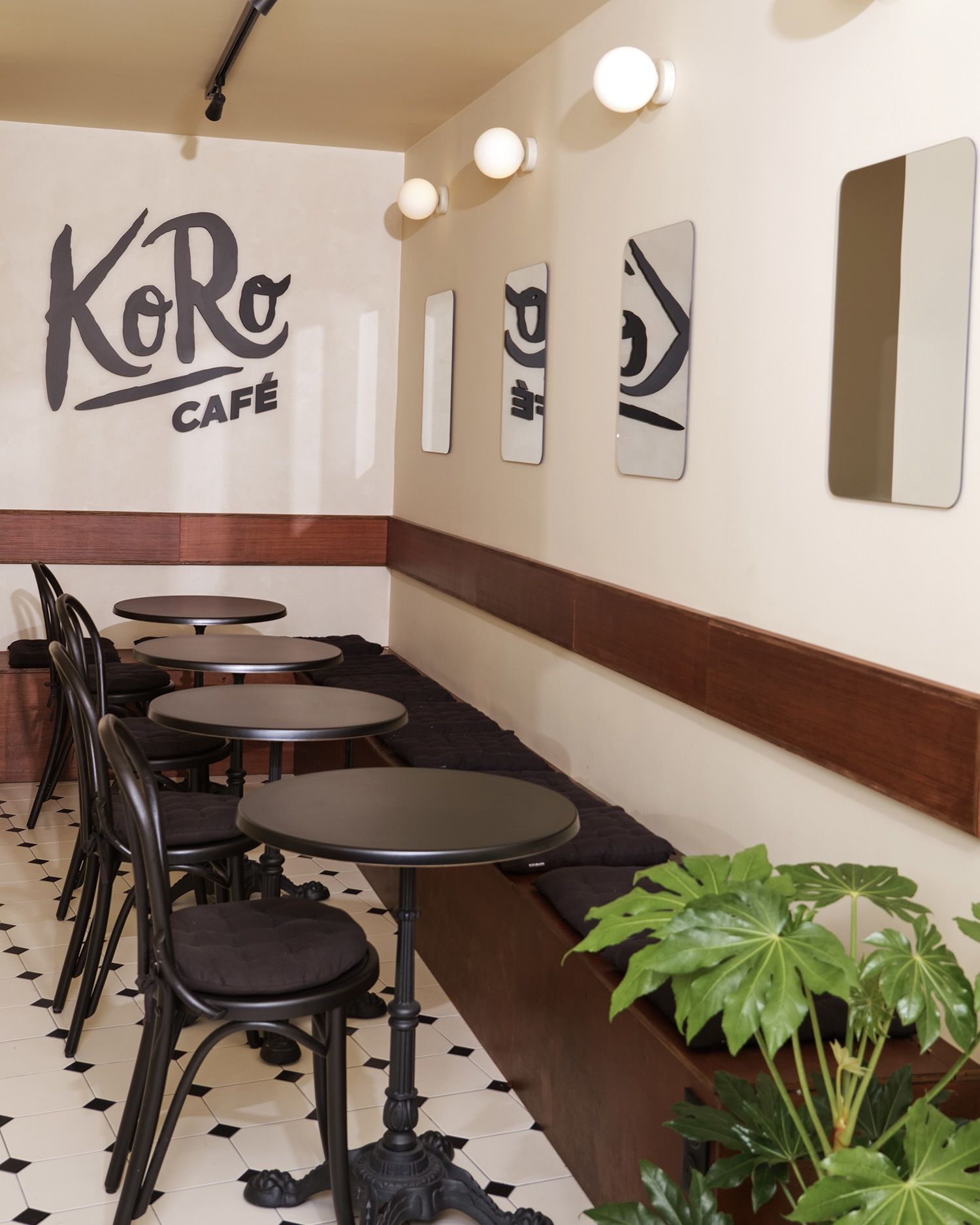 Innenansicht des KoRo Café in Paris mit modernen runden Bistrotischen, schwarzer Bestuhlung und einer gemütlichen Sitzbank vor einer hellen Wand mit Logo-Schriftzug.