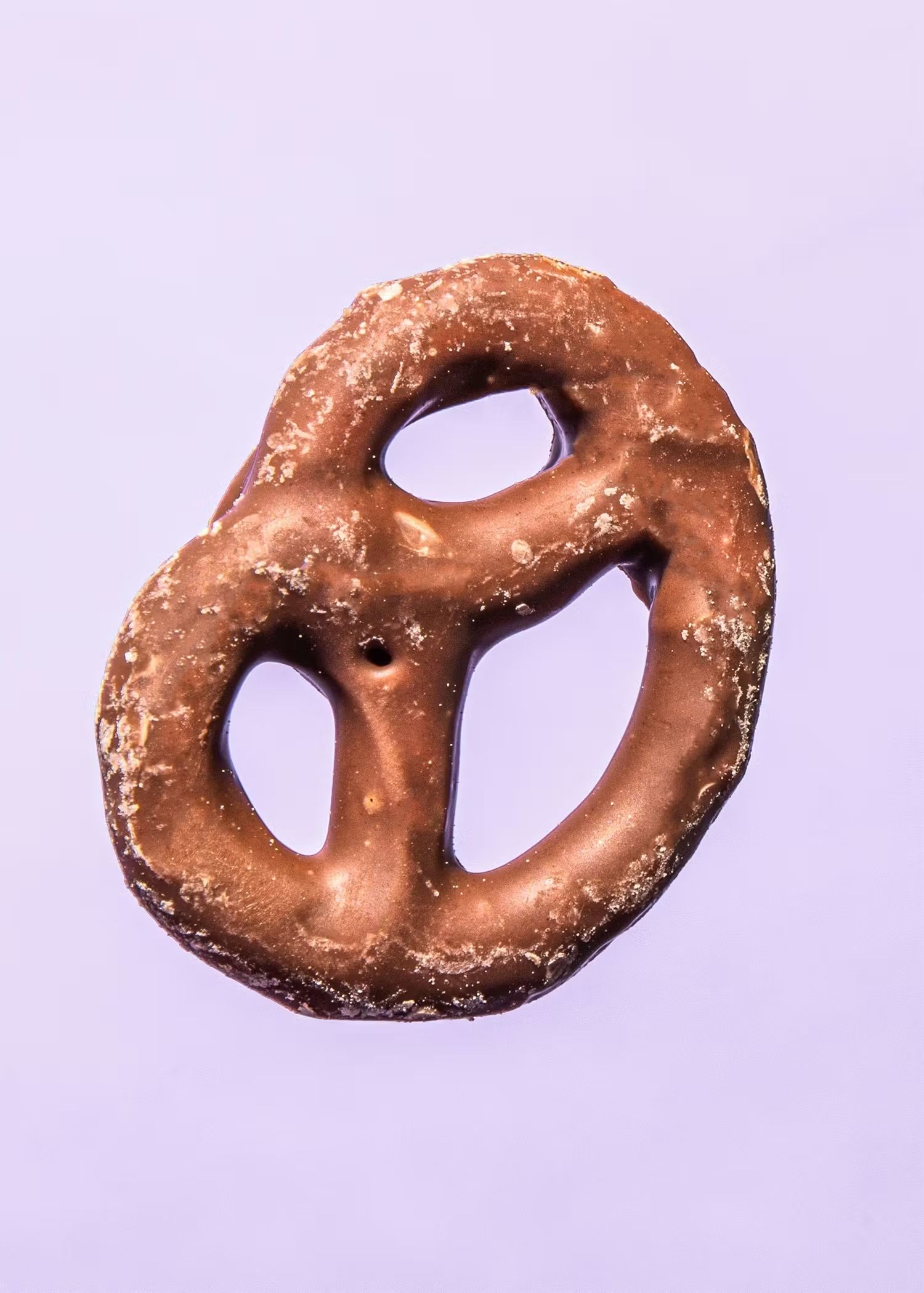 Eine einzelne, mit Vollmilchschokolade überzogene Brezel zentriert vor einem minimalistischen, hellvioletten Hintergrund.