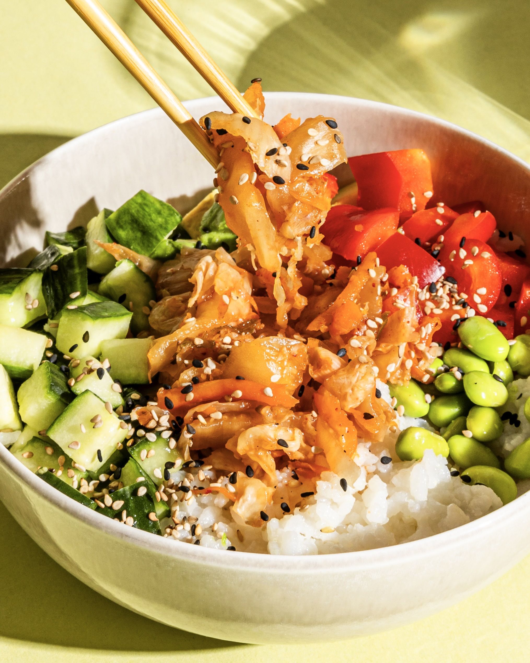 Un bol contenant du riz, du concombre, des edamames et des poivrons, garni de kimchi illustrant un aliment fermenté, saupoudré de sésame.