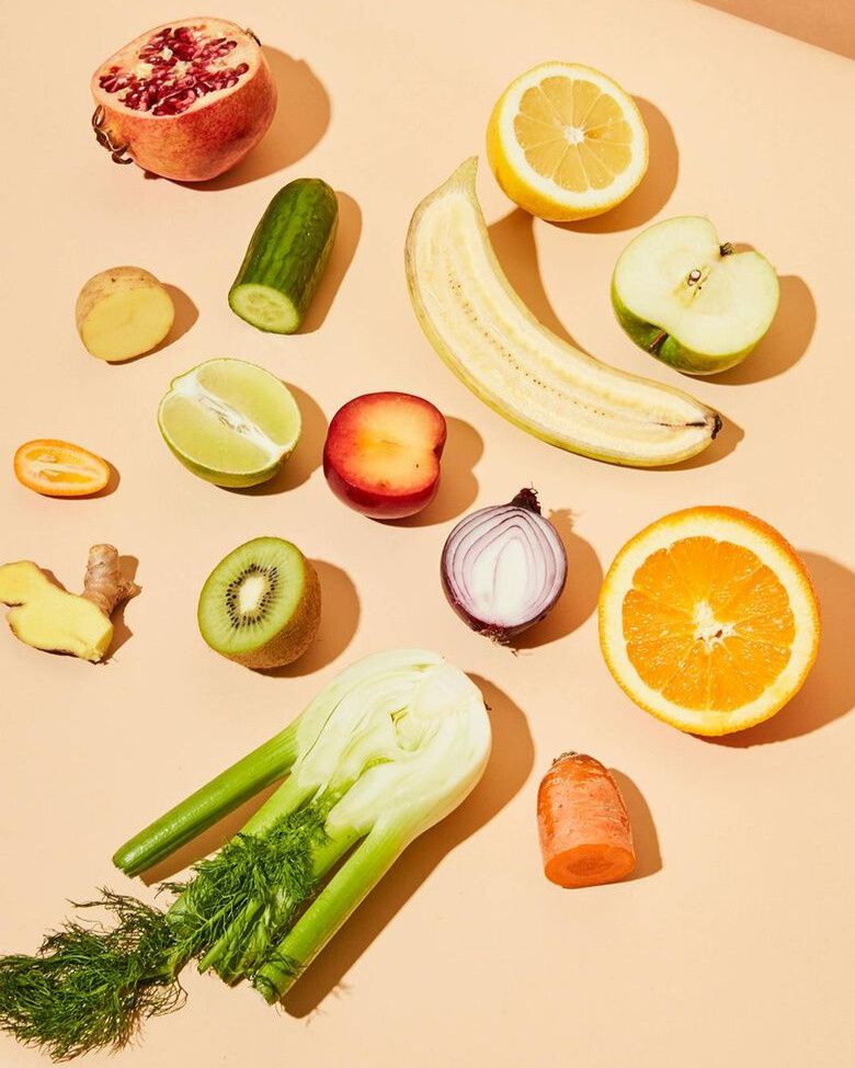  Eine Sammlung von frischem Obst und Gemüse, das in der Mitte durchgeschnitten wurde, liegt auf einem hellen Hintergrund. Von links oben im Uhrzeigersinn sind zu sehen: ein halber Granatapfel, eine Gurke, eine halbe Zitrone, ein halber Apfel, eine halbe Orange, eine Karotte, eine halbe rote Zwiebel, ein Fenchel, eine Kiwi, ein Stück Ingwer, eine halbe Limette, eine Kumquat, eine Kartoffel und eine halbierte Banane. In der Mitte befindet sich eine halbe Nektarine.