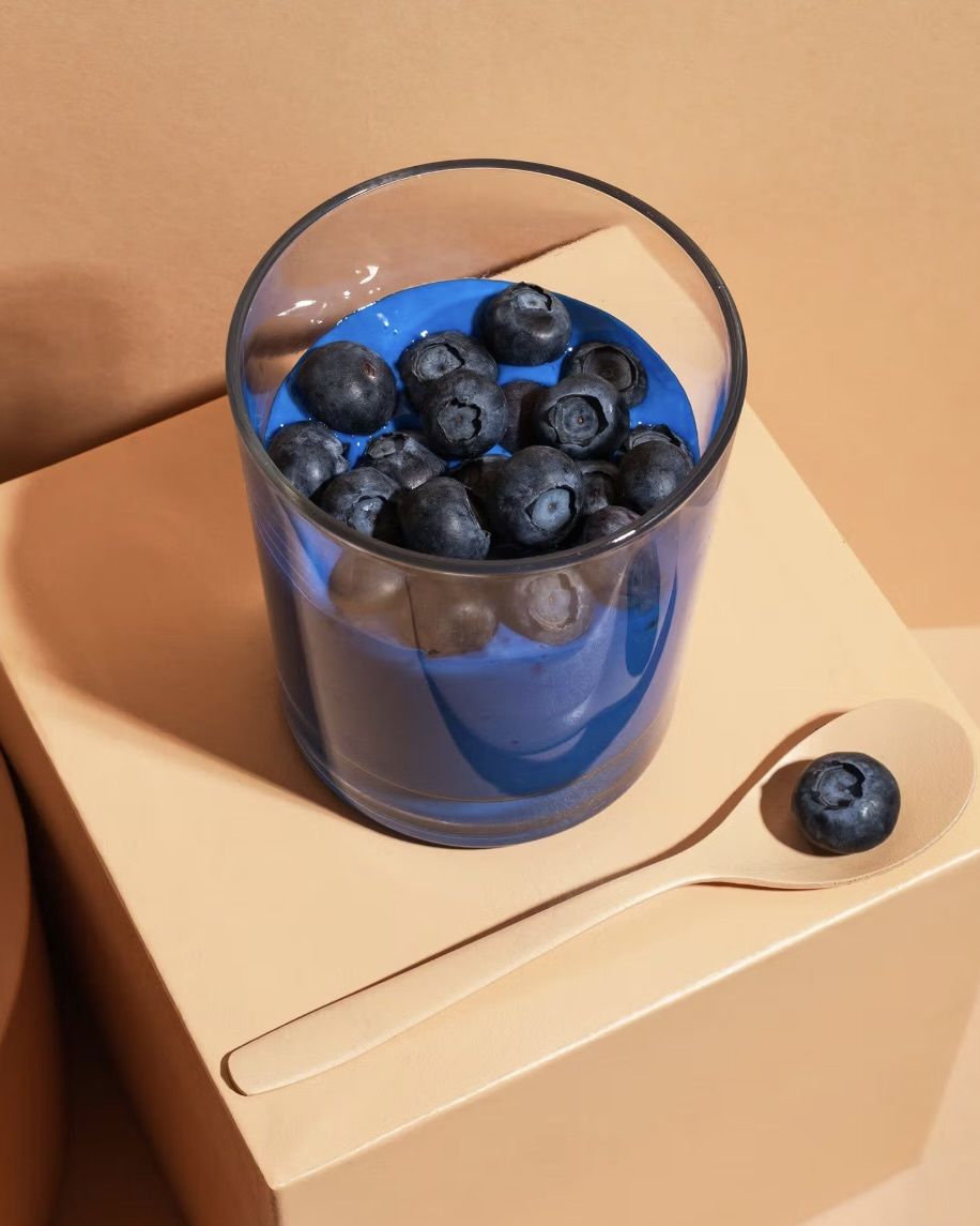 Blauer Spirulina-Smoothie zubereitet mit KoRo Superfood-Pulver, getoppt mit frischen Blaubeeren in einem Glas auf beigem Podest