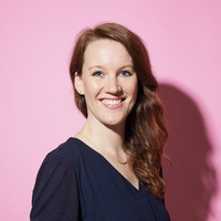 Christina lächelt in die Kamera und steht vor einem hellen Hintergrund