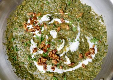 Cremiges veganes Palak Tofu Paneer Curry mit grünem Spinat, goldbraun gebratenem Tofu, gerösteten Cashewkernen, Joghurt und gehackter Petersilie in einer Edelstahlpfanne serviert.