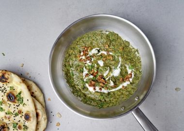 Cremiges veganes Palak Tofu Paneer Curry mit grünem Spinat, goldbraun gebratenem Tofu, gerösteten Cashewkernen, Joghurt und gehackter Petersilie in einer Edelstahlpfanne serviert.