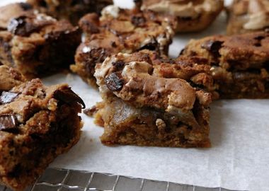 Saftige Kürbis-Blondies mit Schokostückchen und goldbrauner, leicht knuspriger Oberfläche auf Backpapier – herbstliches Gebäck in quadratischen Stücken