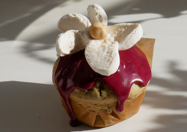 Dekorierter Zitronen-Blaubeer-Muffin mit violettem Heidelbeer-Frosting und weißer Marshmallow-Blüte in Nahaufnahme.