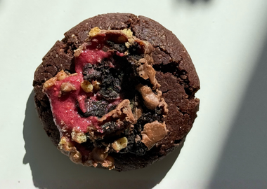 Ein saftiger veganer Schokoladen-Cookie auf hellem Untergrund, großzügig getoppt mit Stücken eines Raspberry Brownie Proteinriegels.