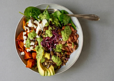 Kürbis-Bowl mit Pinto Bohnen, Hokkaido-Kürbis, Quinoa und Babyspinat auf grauem Hintergrund. Garniert mit Feta, Avocado, Sprossen und gerösteten Kürbiskernen.