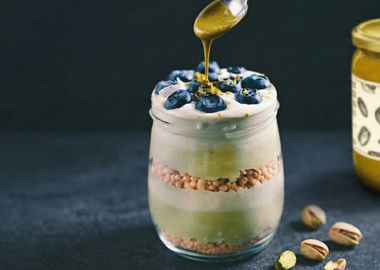Schichtdessert mit Joghurt, Sojacrispies und Blaubeeren, verfeinert mit KoRo Pistazienmus und Pistazienkernen.