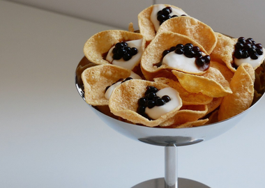 Veganer Vorspeisen-Snack: Knusprige Linsenchips angerichtet mit cremiger Yuzu-Mayonnaise und dunklen Essigperlen in einer edlen Metallschale.
