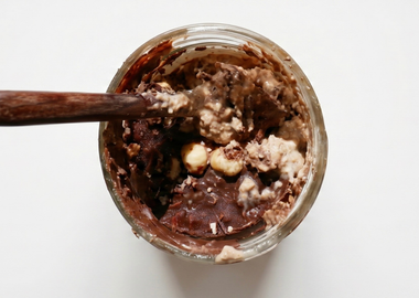 Cremige Schoko-Haselnuss-Overnight-Dinkelflocken im Glas mit ganzen Nüssen und einem Löffel serviert.