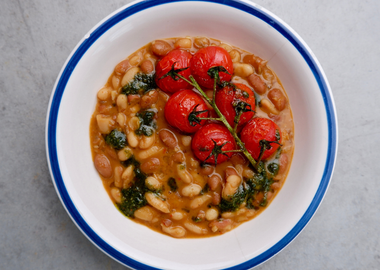 Veganer One-Pot-Bohneneintopf aus weißen und braunen Bohnen, zubereitet mit Olivenöl, Knoblauch und Gewürzen, serviert mit geschmorten Cherrytomaten.