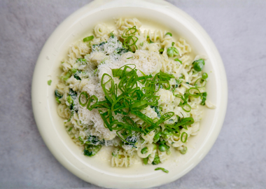 Cremige Pasta al Limone mit Erbsen, geriebenem Parmesan und Frühlingszwiebeln auf einem hellen Teller.