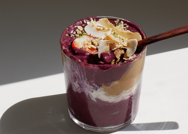 Vegane Acai Bowl im Glas mit Kokosraspeln, Erdbeeren, Hanfsamen und Erdnussbutter im hellen Sonnenlicht.