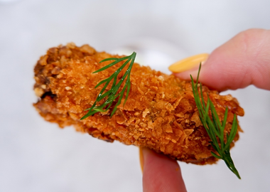 Knusprig frittierte Gewürzgurke (Deep Fried Pickle) mit frischem Dill garniert, serviert als Fingerfood-Snack vor hellem Hintergrund.