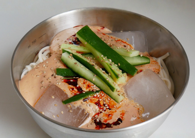 Vegane kalte Nudeln in kalter Tomaten-Chili-Sauce mit Gurken und Sesam in einer Metallschüssel.