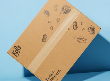 Brauner KoRo Versandkarton mit Produktzeichnungen auf hellblauem Hintergrund, der das "Better. Different." Motto und die Website koro.com zeigt.